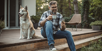 man and dog sitting on a porch looking at mobile device